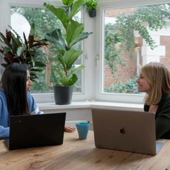 Two people sat at a table with laptops open, having a meeting.