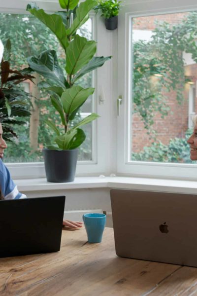 Two people sat at a table with laptops open, having a meeting.